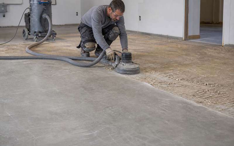 A worker grinding a concrete slab beside a dust extractor.